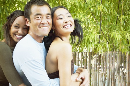 Portrait of two young women and a mid adult man holding each otherの写真素材