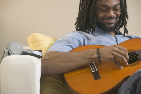 Young man sitting on a couch playing a guitarの写真素材