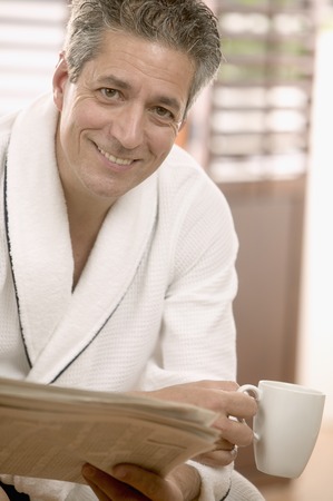 Man sitting holding a coffee cup and a newspaperの写真素材