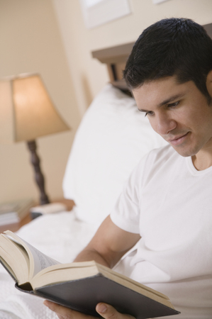 Hispanic man reading book in bedの写真素材