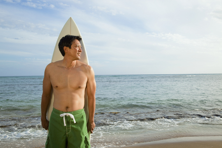 Japanese man with surfboard on beachの写真素材