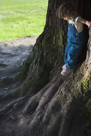 Mixed race girl leaning on tree trunksの写真素材