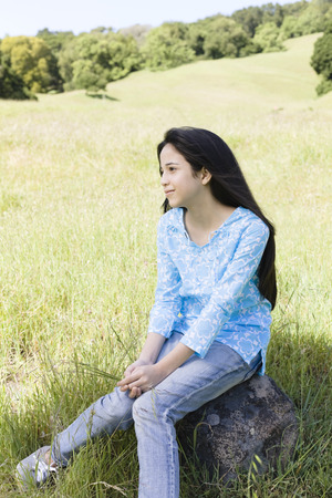 Hispanic girl sitting on rock in fieldの写真素材