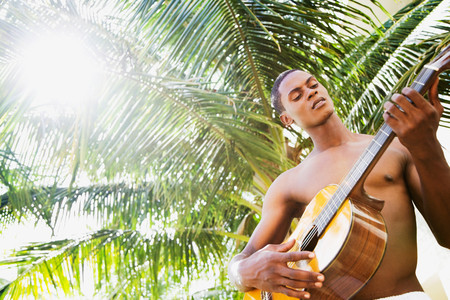 African man playing guitar in front of palm tree