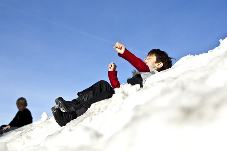 Mixed race boy sledding downhill in snowの写真素材