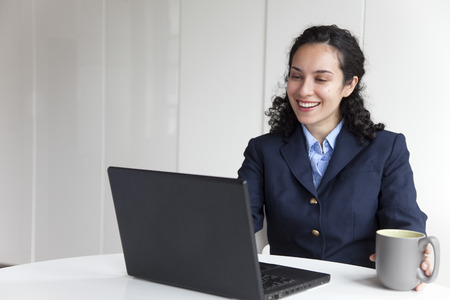 Hispanic businesswoman using laptop and drinking coffee