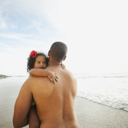 Black father carrying daughter on beachの写真素材