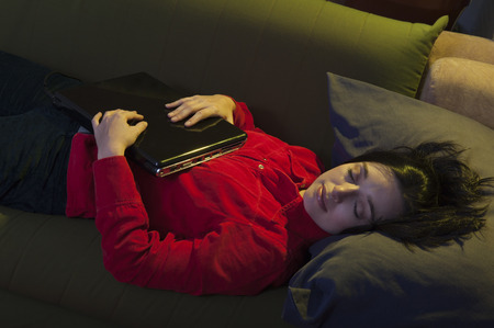Hispanic woman sleeping on sofa holding laptop