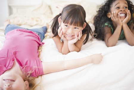 Smiling girls laying on bed togetherの写真素材