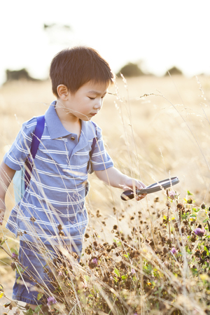 Chinese boy looking at flowers with magnifying glassの写真素材
