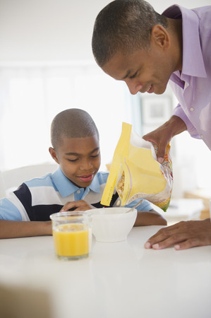 Mixed race man pouring cereal for sonの写真素材