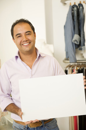 Hispanic man holding blank sign in clothing storeの写真素材