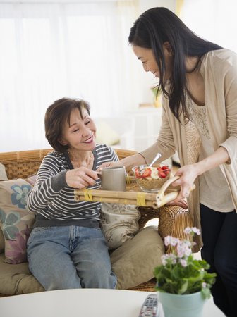 Japanese daughter bringing mother breakfast on a trayの写真素材