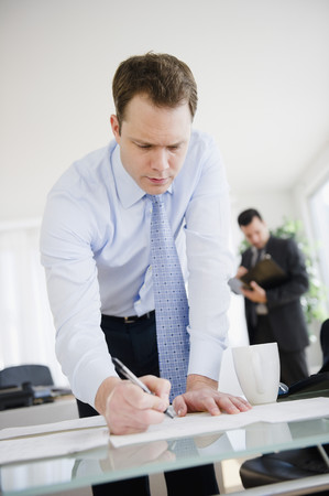 Caucasian businessman leaning on desk and writingの写真素材
