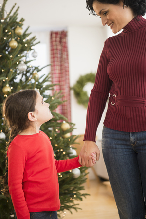 Mother and daughter holding hands by Christmas treeの写真素材
