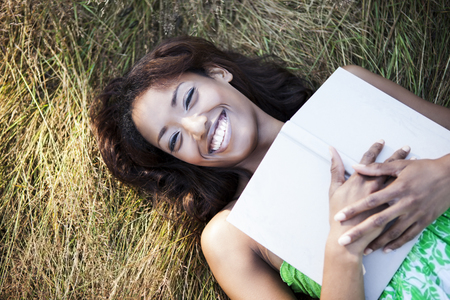 Mixed race woman holding book in grassの写真素材