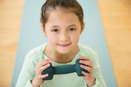 Mixed race girl holding weight on yoga matの写真素材