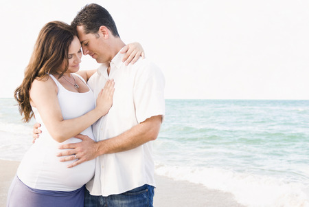 Caucasian man hugging pregnant wife on beachの写真素材