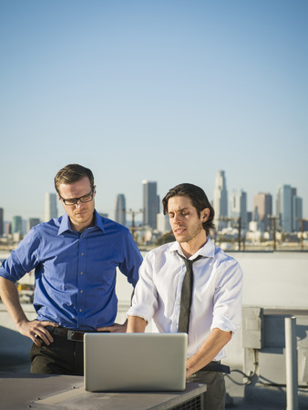 Businessmen using laptop on urban rooftopの写真素材