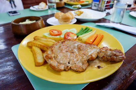 Pork steak with vegetables in yellow plate.の写真素材