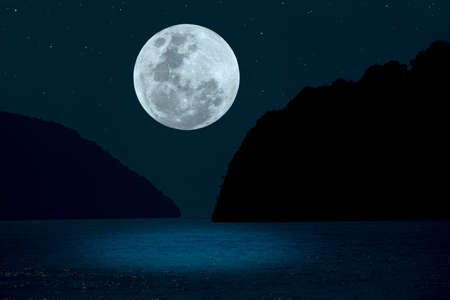 Full moon on sky over silhouette mountains and sea.の写真素材