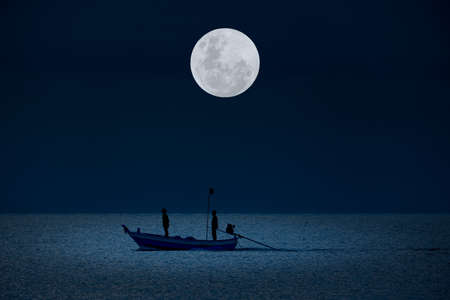 Full moon in the sky with silhouettes people on boat in water at night.の写真素材