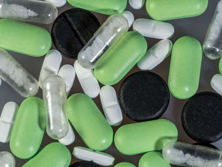White, green and black tablets of various shapes, transparent capsules with powder on a flat surface. Medicines for different diseases on a gray background.の写真素材