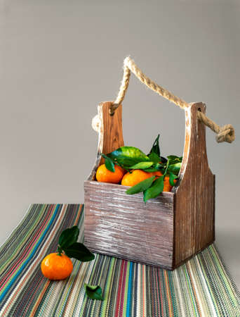A small box with handles filled with tangerines. On tangerines leaves. A box is standing on a colorful napkin. Bright fruit background.の写真素材