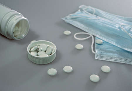 Tablets or vitamins are in a plastic container, in the lid of the container and on the table. Nearby are medical masks. Photo for backgroundの写真素材