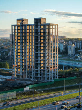 The sun's rays illuminate the frame of a multi-storey building under construction. The highway...