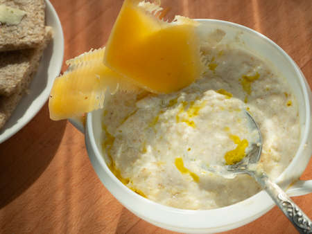 Milk porridge with vegetable oil. Spoon in a plate with porridge. On the porridge lies chopped cheese. On a plate are crispy snacks. Diet breakfast.の写真素材