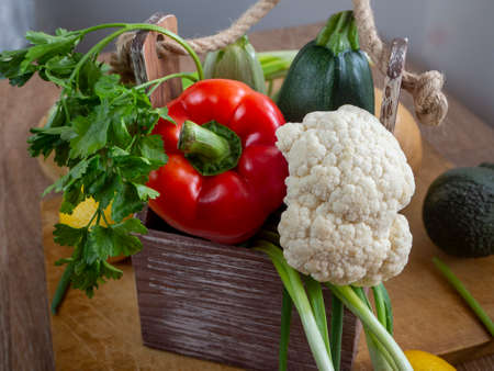 Zucchini, bell pepper, cauliflower and greens are stacked in a wooden box with handles. Vegetables...