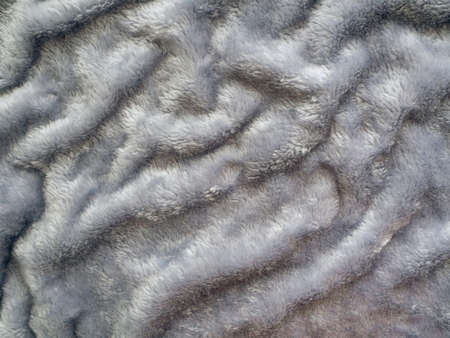 Gray fur with a small pile lies in waves on the surface. Background with faux fur.