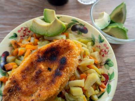 Vegetable side dish, avocado and meat cutlet for lunch or dinner. The plate stands on a wooden...