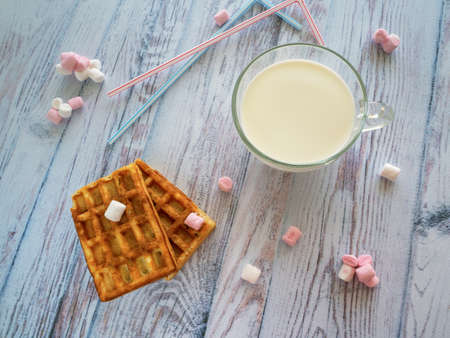 Breakfast for the child with milk, cookies and sweets. On a wooden surface is a cup of milk. Rectangular cookies, sweets and tubule for drinks on the table.の写真素材