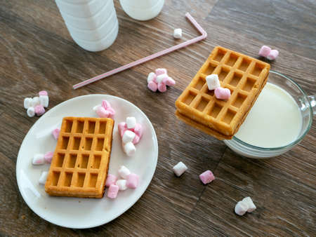 On the table is a cup of milk or a milk drink. On a cup of cookies. Rectangular cookies and sweets lie on a saucer. On the table are bottles of milk, are sweets and a straw for drinks.の写真素材