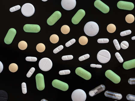 Medical preparations on a black background. Pills and capsules of different colors create a pattern....