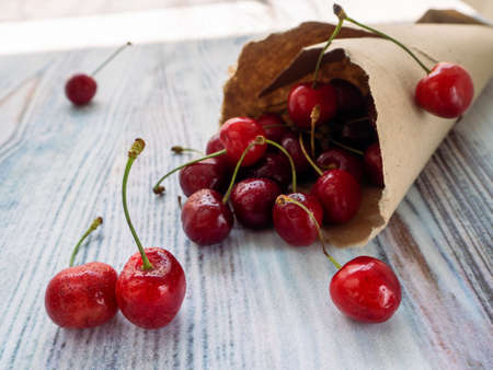 Several berries of ripe cherries on a wooden table in drops of water. The rest of the berries are in a paper bag. Background with cherries.の写真素材