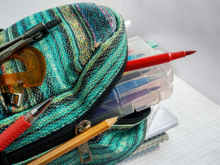 School bag is open. It contains notebooks, a pencil case, pens, pencils, felt-tip pens, compasses...