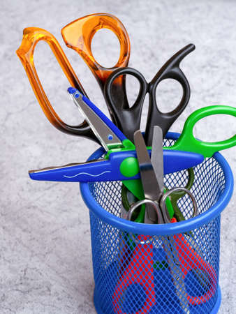 Scissors of different sizes and for different jobs are in a mesh container. Children's scissors with a wavy edge lie across the container.の写真素材
