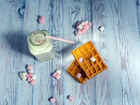 Cookies with a checkered texture, sweets and milk in a bottle on a light wooden surface.