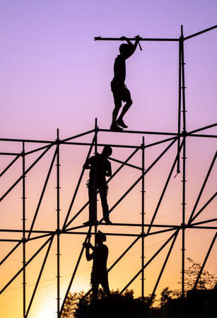 Silhouettes of workers against the sunset sky. Workers stand at different heights of the metal structure and dismantle the frame.の写真素材