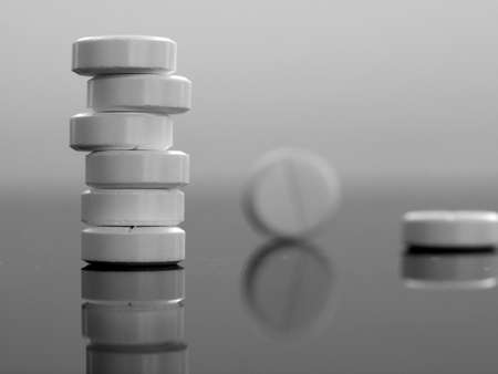 Black and white monochrome background with round pills close-up. The pills are stacked and individually on a black mirror surface. Medical background with medicines.の写真素材