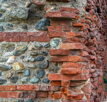 The crumbling walls of an antique building. The walls are made of large, uneven red bricks and stones of various sizes. Stone vintage background.の写真素材