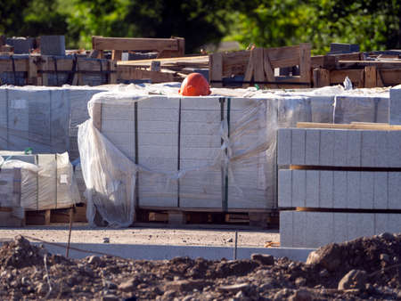Curbstones are stacked in piles. They are wearing a construction helmet. Construction road works for...