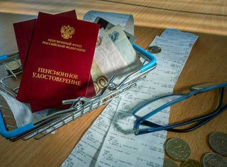 Pension certificates, Russian money, sales receipts, a shopping basket and glasses are on the table. Conceptual background with Russian pensioner documents and rubles.の写真素材