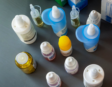 Eye drops in glass and plastic bottles with nozzles for instillation. View from above. There are other medications nearby. Medical background with medicines for eye treatment.の写真素材