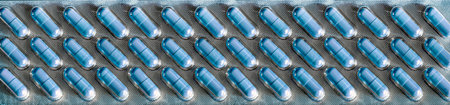 Light blue pills are packed in rows in a long transparent blister that takes up the entire...