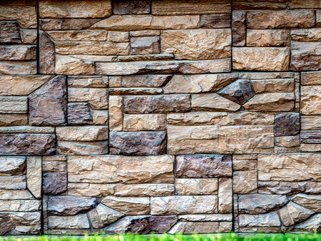 A stone wall of geometric blocks of varying sizes and shapes rises above a narrow strip of grass....