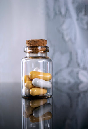 Yellow and white capsules are in the bottle. The bottle stands on a black glass surface. Space for...